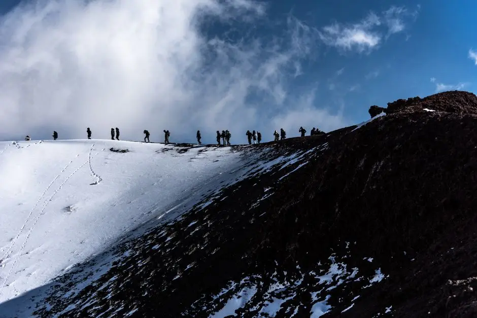 Adventurers trekking the snowy slopes of Mount Etna in Sicily, Italy under a dramatic sky.
