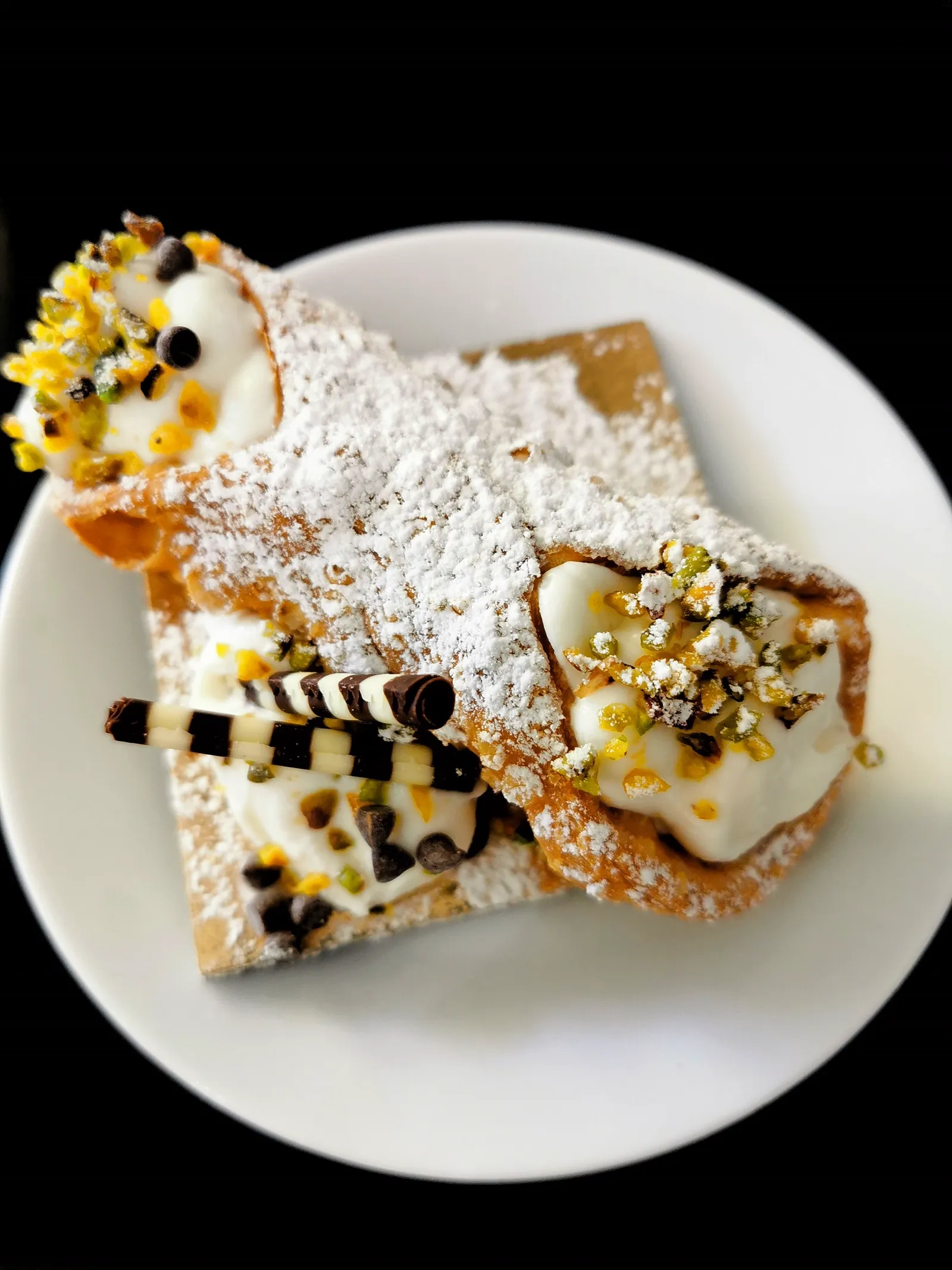 Sicilian cannoli with a crisp shell, filled with ricotta cream, dusted with pistachios and powdered sugar.
