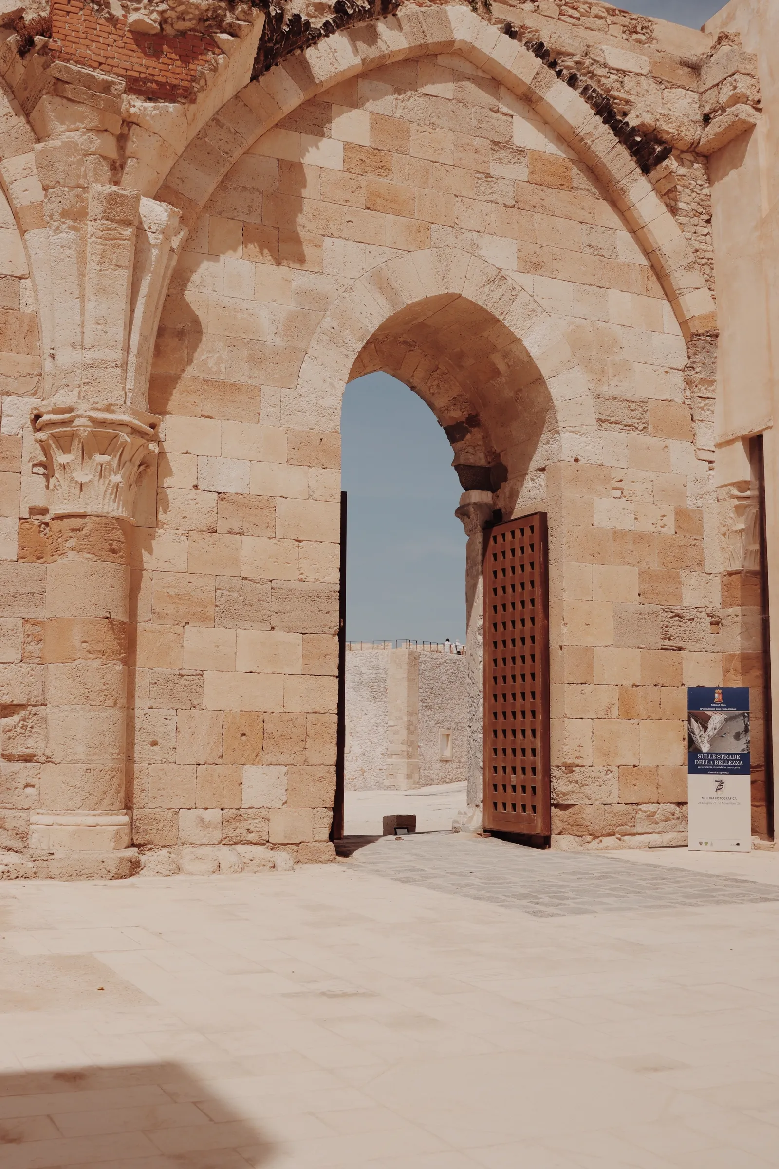 The pointed stone archway entrance of Castello Maniace in Siracusa, with its heavy wooden gate open toward the fortress courtyard.