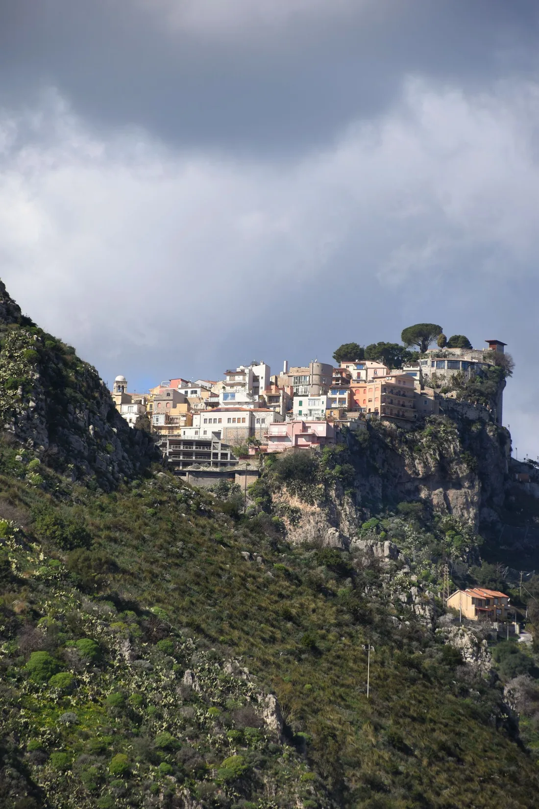 Castelmola village perched dramatically on a rocky peak above Taormina, Sicily, with terraced hillsides below.