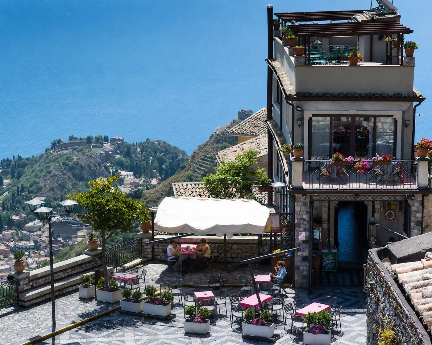 The terrace of Antico Caffè San Giorgio in Castelmola, with tables overlooking Taormina and the sea far below