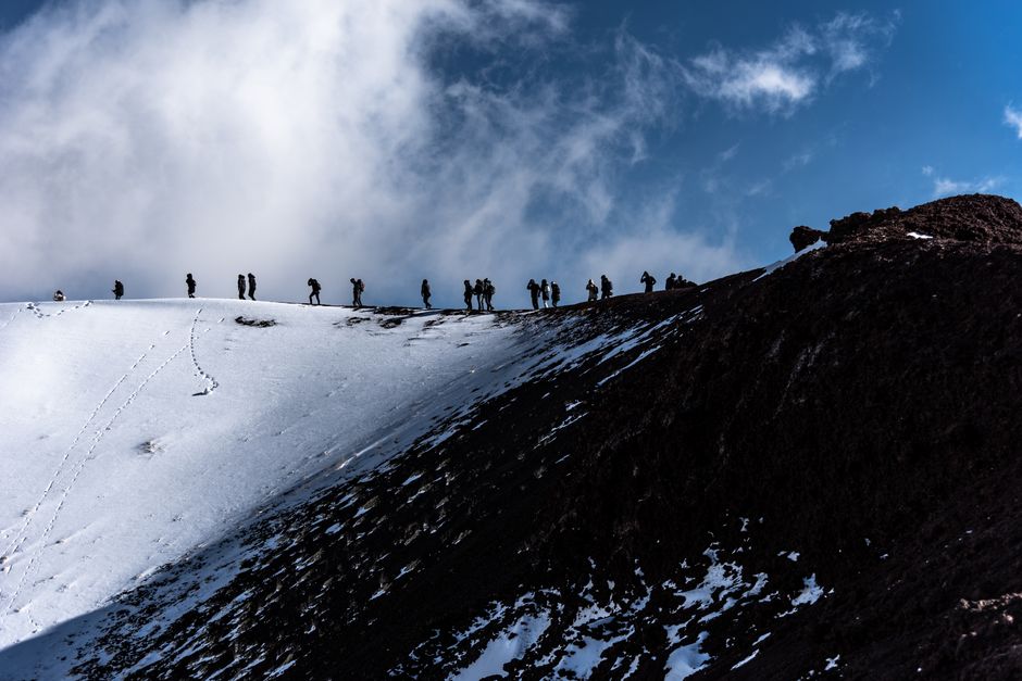 Adventurers trekking the snowy slopes of Mount Etna in Sicily, Italy under a dramatic sky.