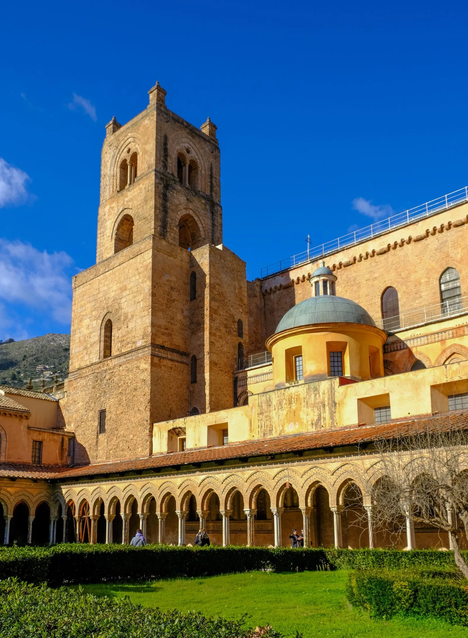 The honey-colored stone exterior of Monreale Cathedral with its Norman bell tower, seen from the cloister garden below.