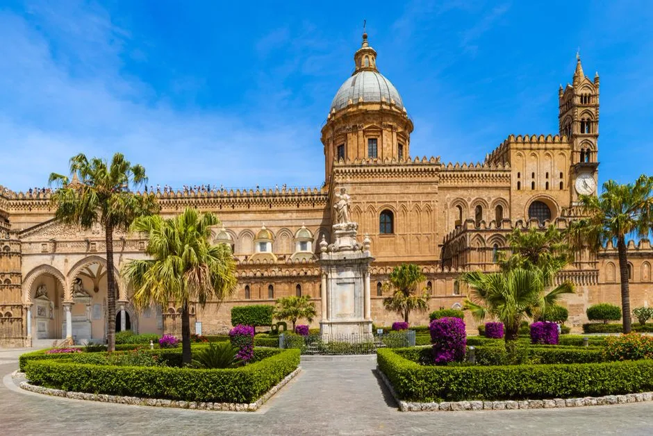 The Cathedral of Palermo, with its distinctive dome, bell tower, and crenellated Arab-Norman battlements, seen from the garden square in front of it.