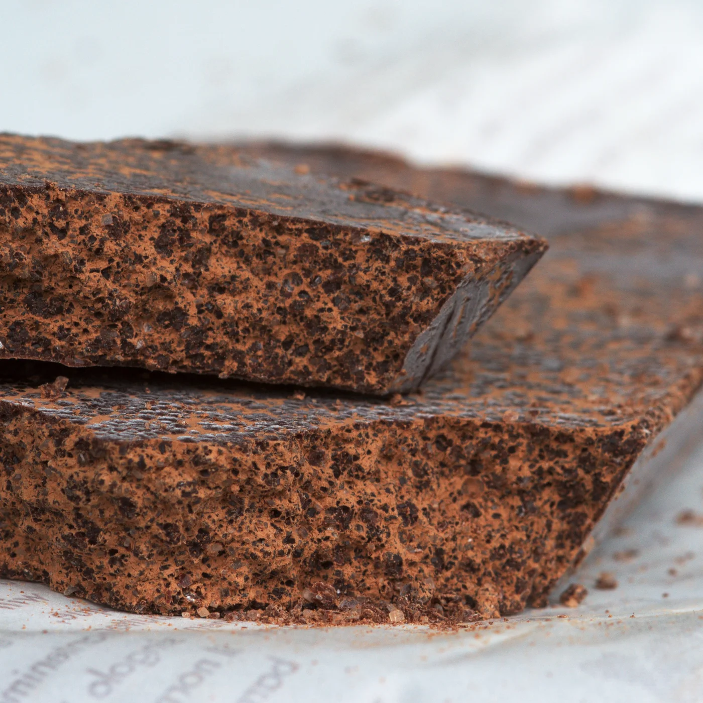Two broken bars of Cioccolato di Modica showing a visibly grainy, matte fracture with fine sugar crystals.