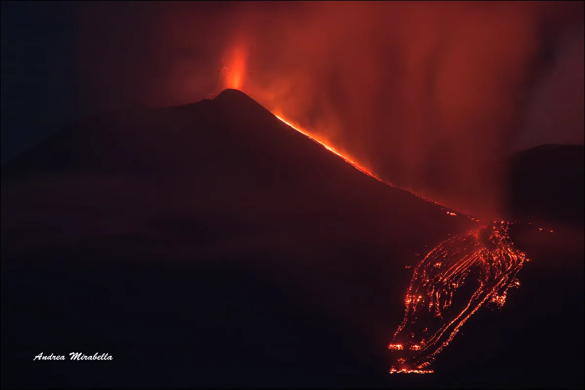 A nighttime lava fountain and lava flows on Mount Etna, the sky lit red by the volcanic glow.