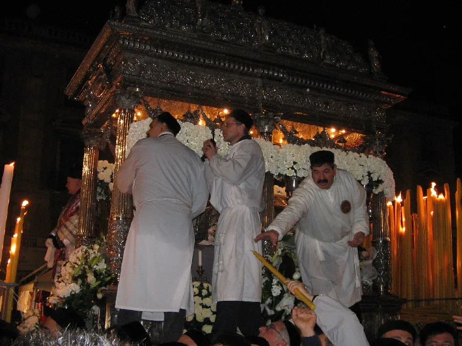 The silver reliquary shrine (fercolo) of Saint Agatha, surrounded by devotees in white robes by candlelight.