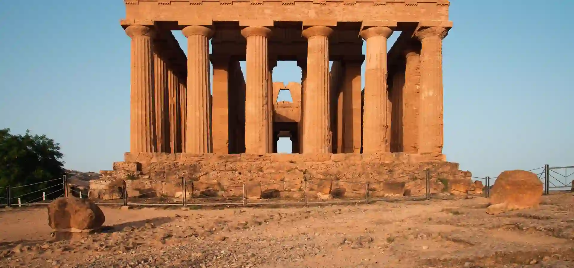 The Temple of Concordia in the Valle dei Templi, Agrigento, glowing warm orange at golden hour against a clear blue sky.