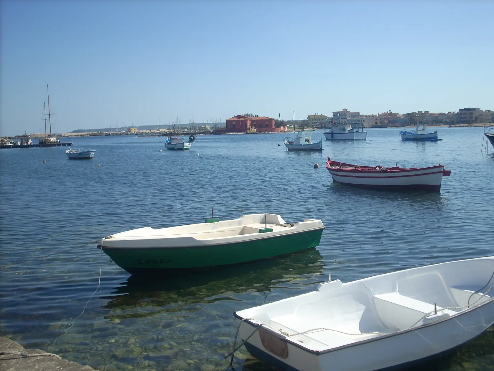 Small fishing boats moored in the shallow harbour at Marzamemi in Sicily, with the low buildings of the old tuna fishery along the shore behind