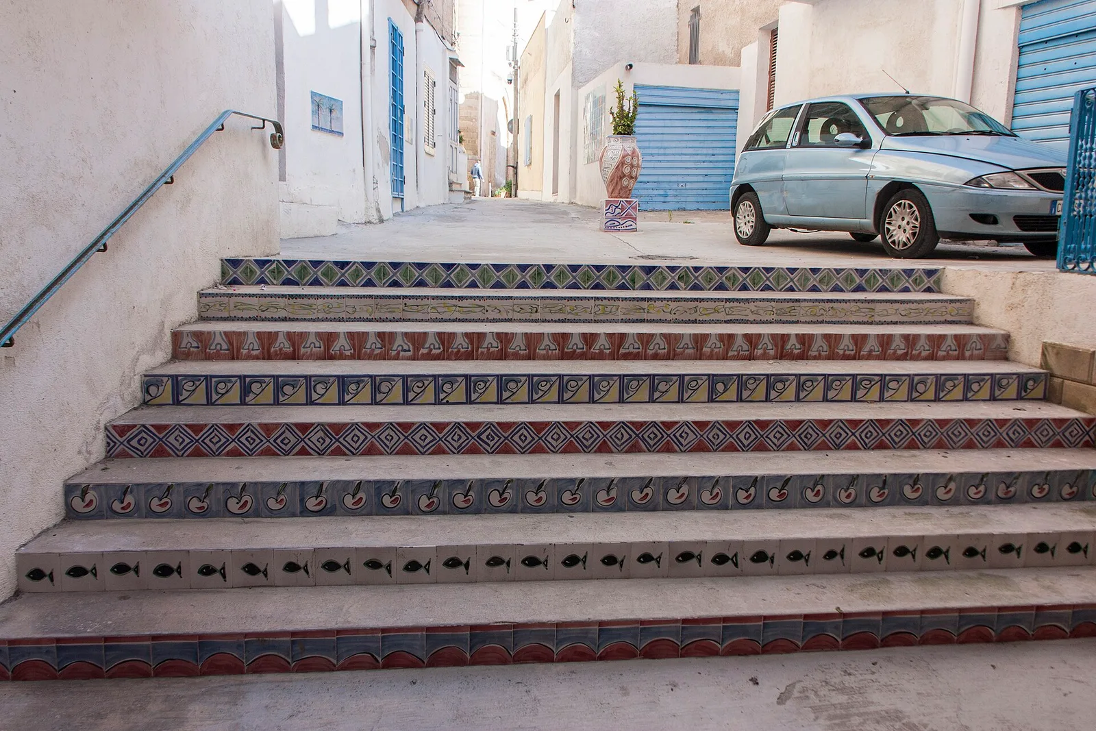 A flight of steps in the Kasbah of Mazara del Vallo, each riser faced in a different hand-painted ceramic pattern — fish, cherries, geometric borders