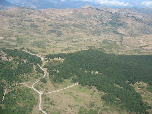 Aerial view of the forested Nebrodi mountains with a small lake and the town of Mistretta in the background.