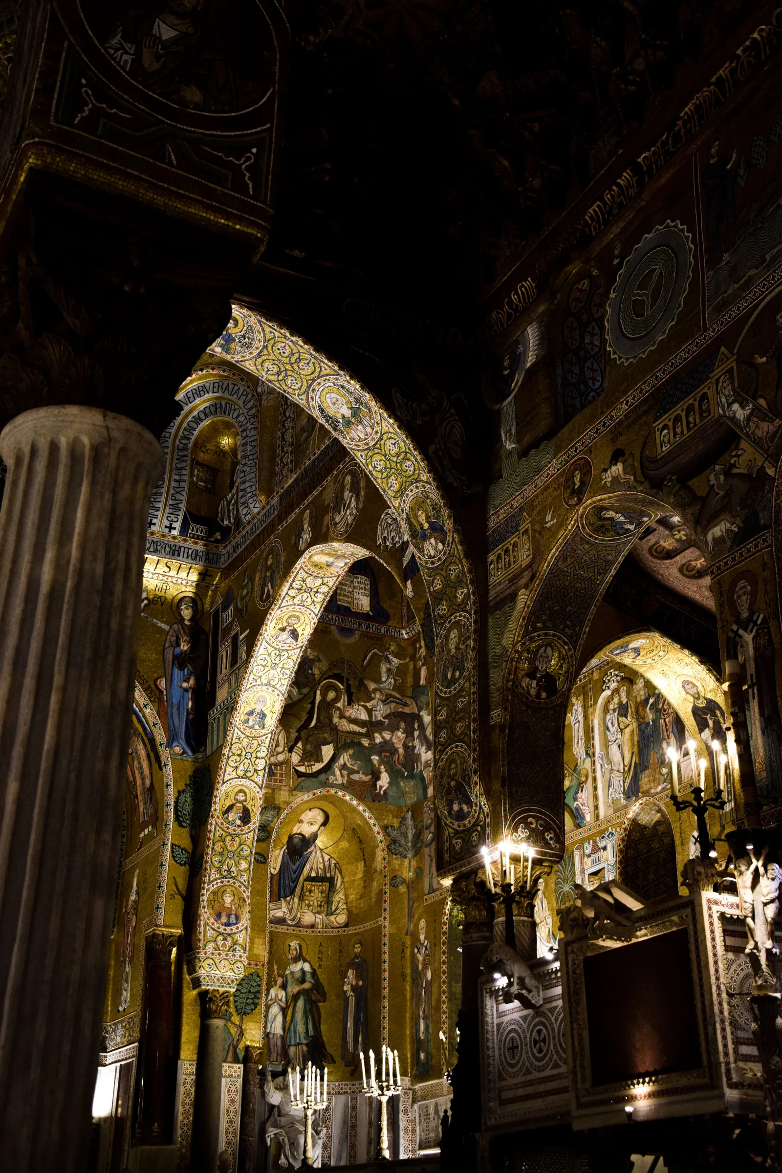 Gold Byzantine mosaics covering the arches and walls of the Cappella Palatina in Palermo, lit by candelabra, showing biblical scenes and Arabic muqarnas decoration.