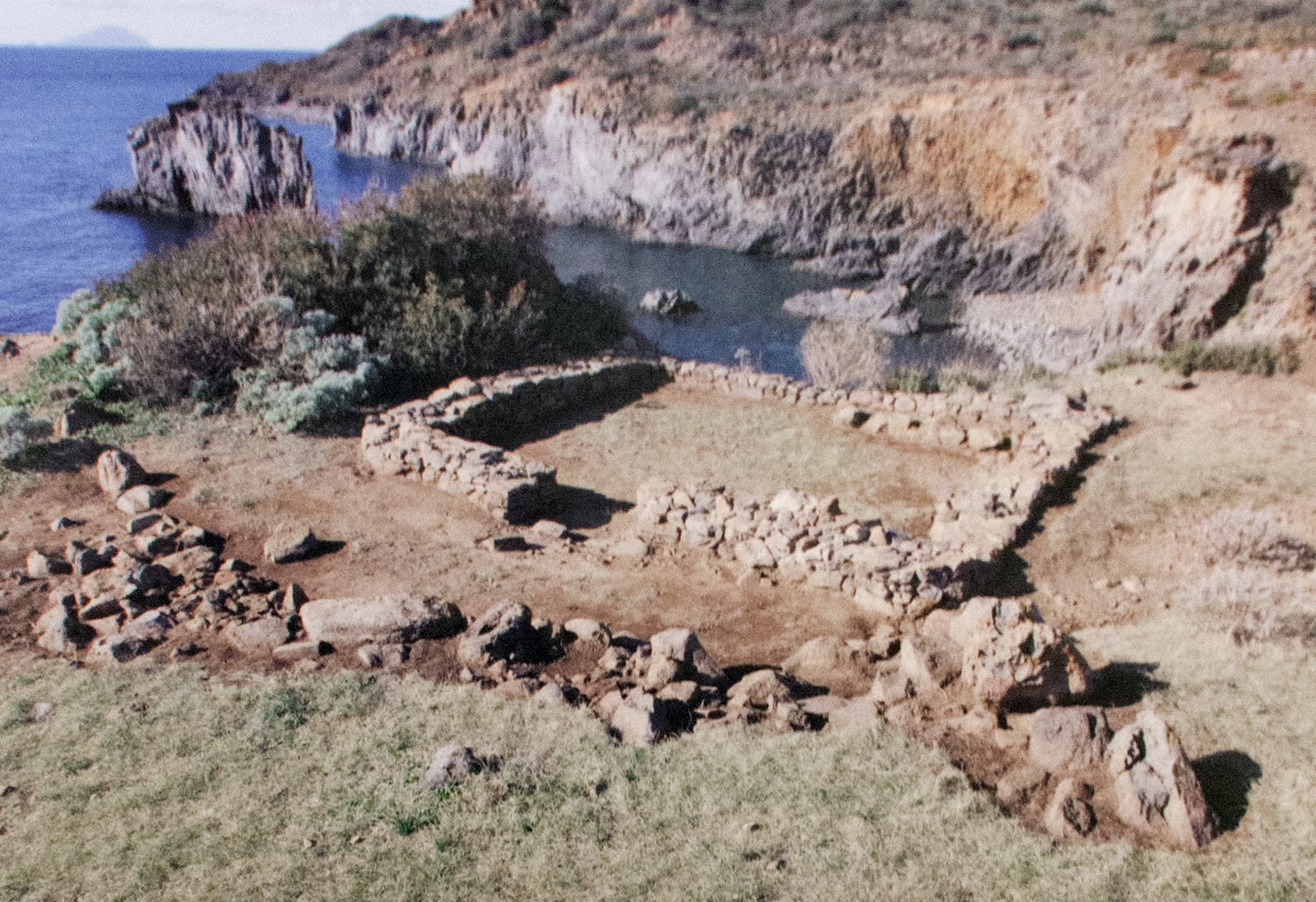 The stone foundations of the Bronze Age prehistoric village at Punta Milazzese on Panarea, overlooking the cliffs and turquoise cove of Cala Junco.