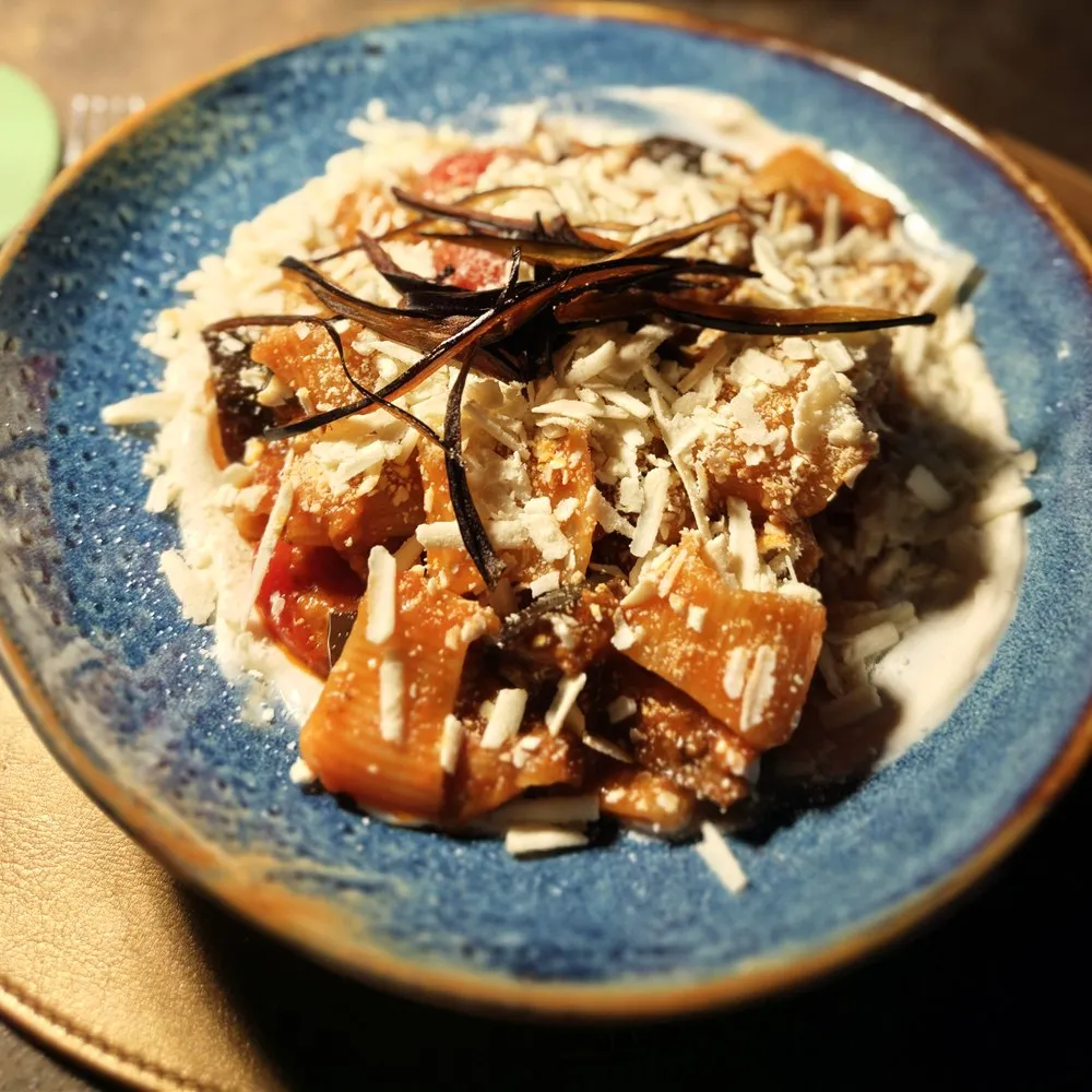 A plate of homemade Pasta alla Norma on a blue ceramic plate, with rigatoni, fried eggplant slices, tomato sauce, and grated ricotta salata.