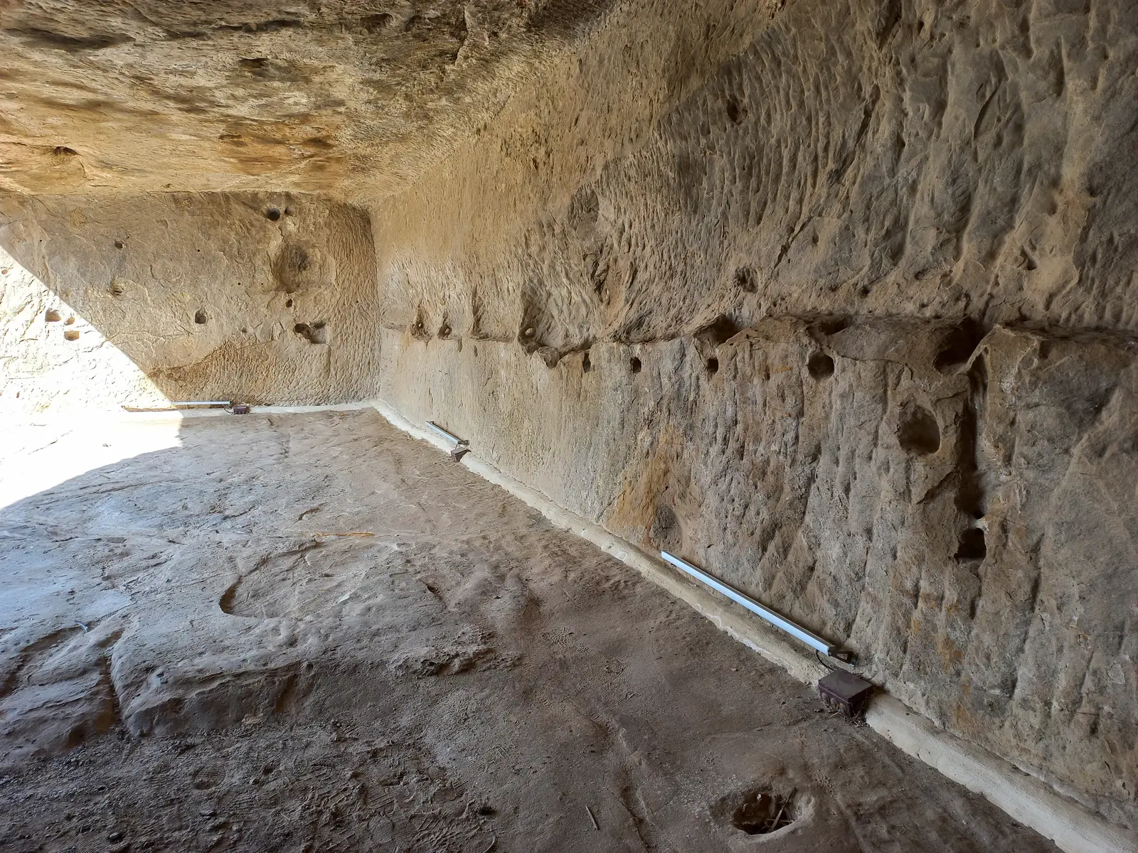 A rock-cut chamber at Sperlinga in Sicily, its sandstone walls pierced with rows of small square niches, part of the village's cave dwellings