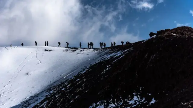 Adventurers trekking the snowy slopes of Mount Etna in Sicily, Italy under a dramatic sky.