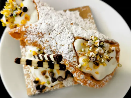 Sicilian cannoli with a crisp shell, filled with ricotta cream, dusted with pistachios and powdered sugar.