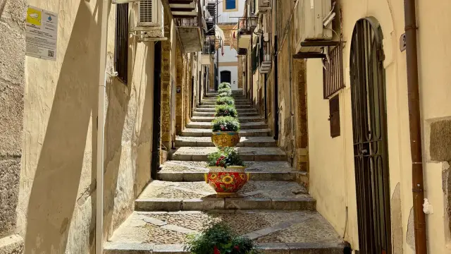 A stepped alley in Castelbuono's old town, lined with hand-painted ceramic pots and stone stairs leading up toward the Madonie mountains.