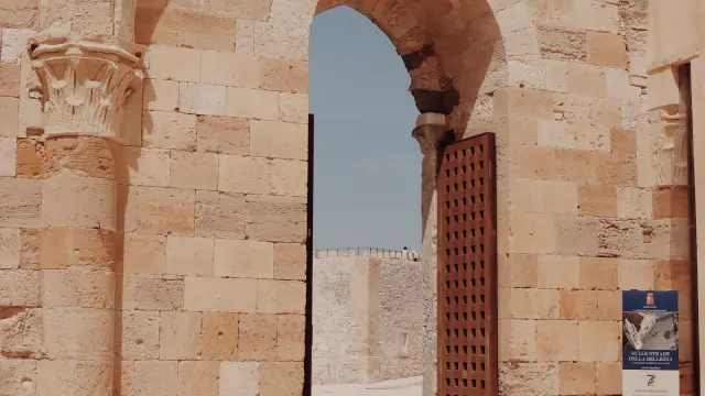 The pointed stone archway entrance of Castello Maniace in Siracusa, with its heavy wooden gate open toward the fortress courtyard.