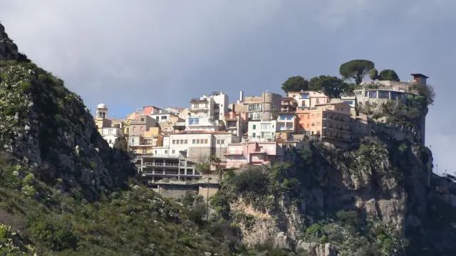 Castelmola village perched dramatically on a rocky peak above Taormina, Sicily, with terraced hillsides below.