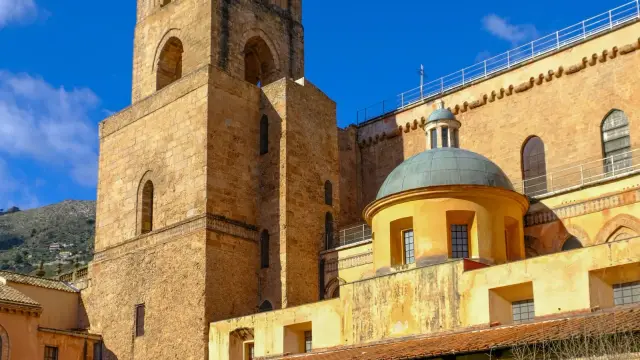 The honey-colored stone exterior of Monreale Cathedral with its Norman bell tower, seen from the cloister garden below.
