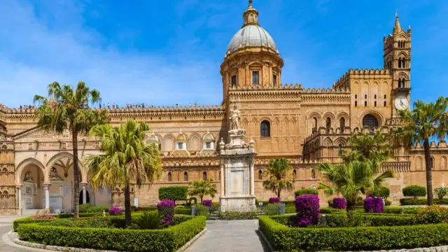 The Cathedral of Palermo, with its distinctive dome, bell tower, and crenellated Arab-Norman battlements, seen from the garden square in front of it.