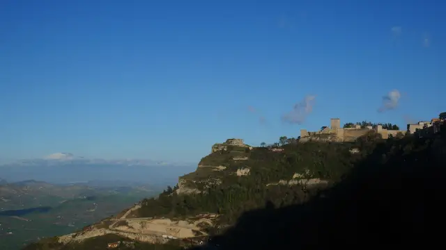 The Castello di Lombardia in Enna, Sicily, standing along a high rocky ridge with the inland valleys and distant mountains of central Sicily spread out far below under a clear sky.