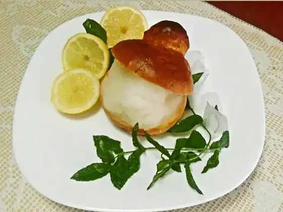 Lemon granita served inside a split brioche col tuppo, on a white plate with lemon slices and mint.