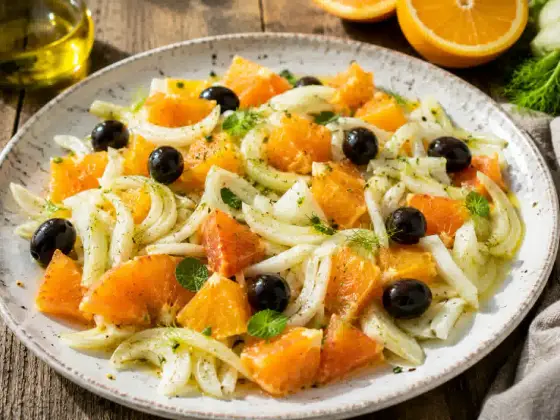 A Sicilian orange and fennel salad on a rustic plate, with thin slices of blood orange and raw fennel, black olives, and a drizzle of olive oil, photographed from above.