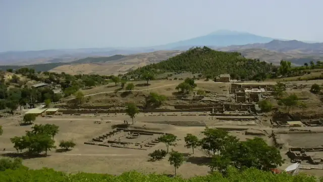 A wide view over the excavated ruins of Morgantina's agora and theater from a hillside, with Mount Etna visible on the horizon.