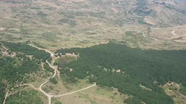 Aerial view of the forested Nebrodi mountains with a small lake and the town of Mistretta in the background.
