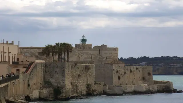 Castello Maniace at the tip of Ortigia in Syracuse, with palm trees and the sea in the foreground.