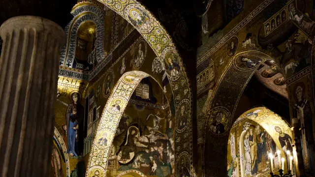 Gold Byzantine mosaics covering the arches and walls of the Cappella Palatina in Palermo, lit by candelabra, showing biblical scenes and Arabic muqarnas decoration.
