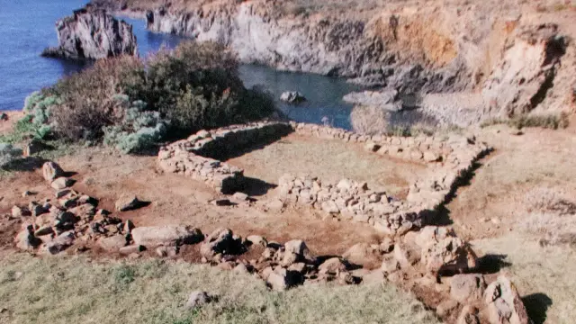 The stone foundations of the Bronze Age prehistoric village at Punta Milazzese on Panarea, overlooking the cliffs and turquoise cove of Cala Junco.