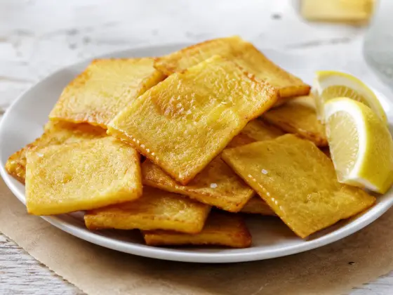 Thin, golden fried panelle slices on a white plate, with lemon wedges on the side.