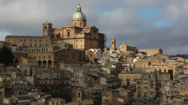 The cathedral of Piazza Armerina in Sicily rising above the tightly stacked ochre houses of the old town on its hillside, its green dome catching the light under a heavy sky.