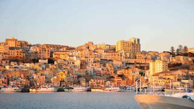 The town of Sciacca in Sicily seen from the water at golden hour, its honey-coloured houses stacked up the hillside above the harbour, with the fishing fleet moored along the quay in the foreground.