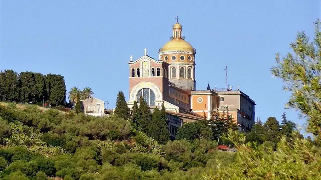 The sanctuary of the Black Madonna at Tindari in Sicily, its golden dome rising above a wooded hillside against a clear blue sky.