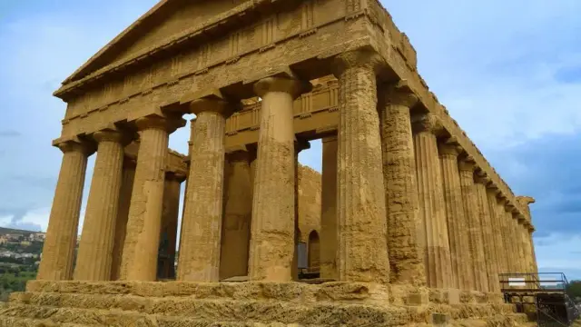 Stunning view of the Temple of Concordia, a well-preserved ancient Greek temple in Agrigento, Sicily, with golden stone, Doric columns, and a blue sky, shot from a low angle.