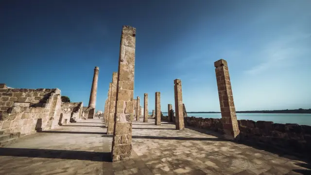 The ancient stone pillars of the Tonnara di Vendicari standing along the shoreline of the nature reserve under a clear blue sky.