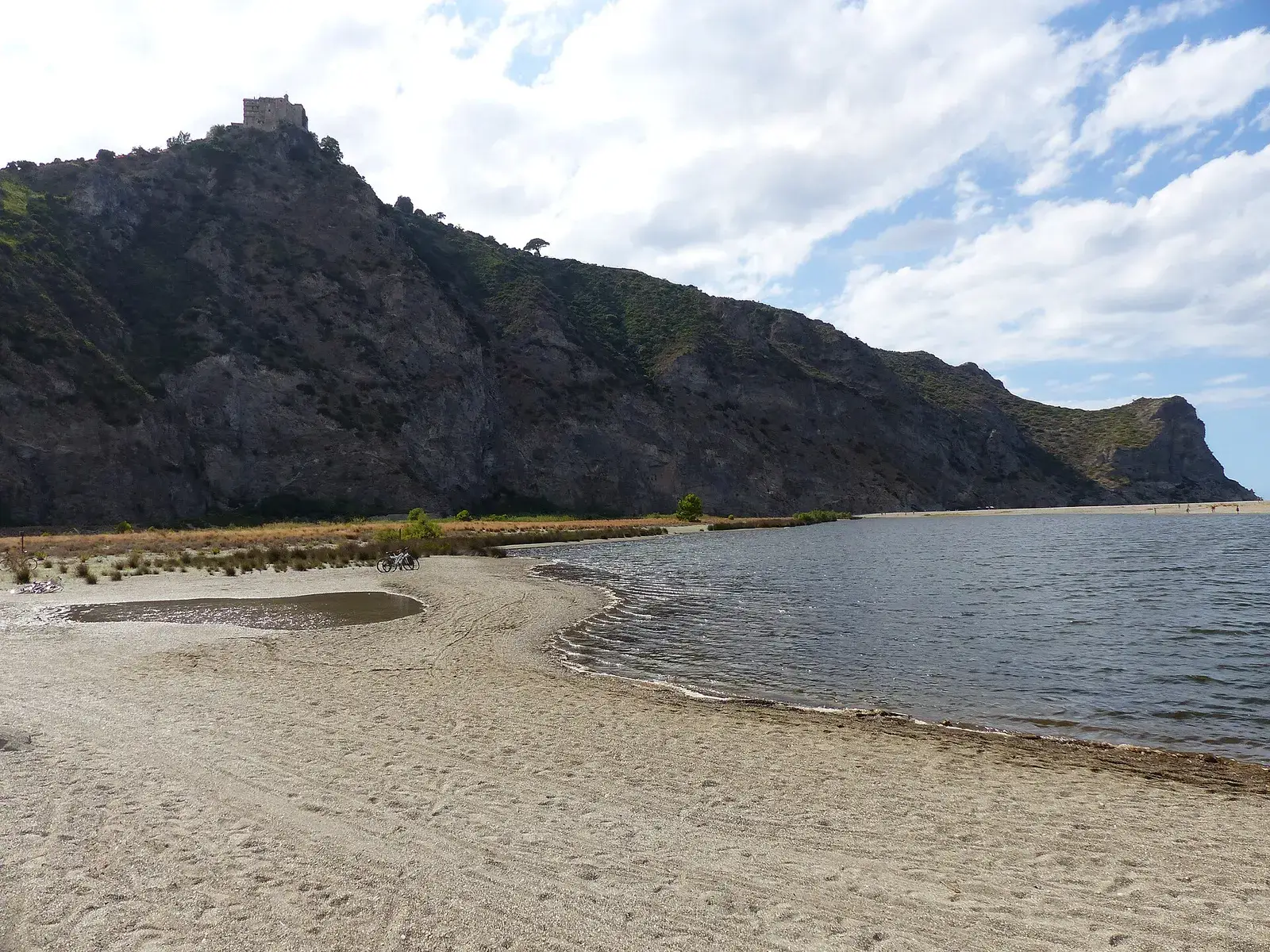 The sandy lagoons of Marinello at the foot of the Tindari headland, with the rocky promontory rising behind and the sanctuary visible on top