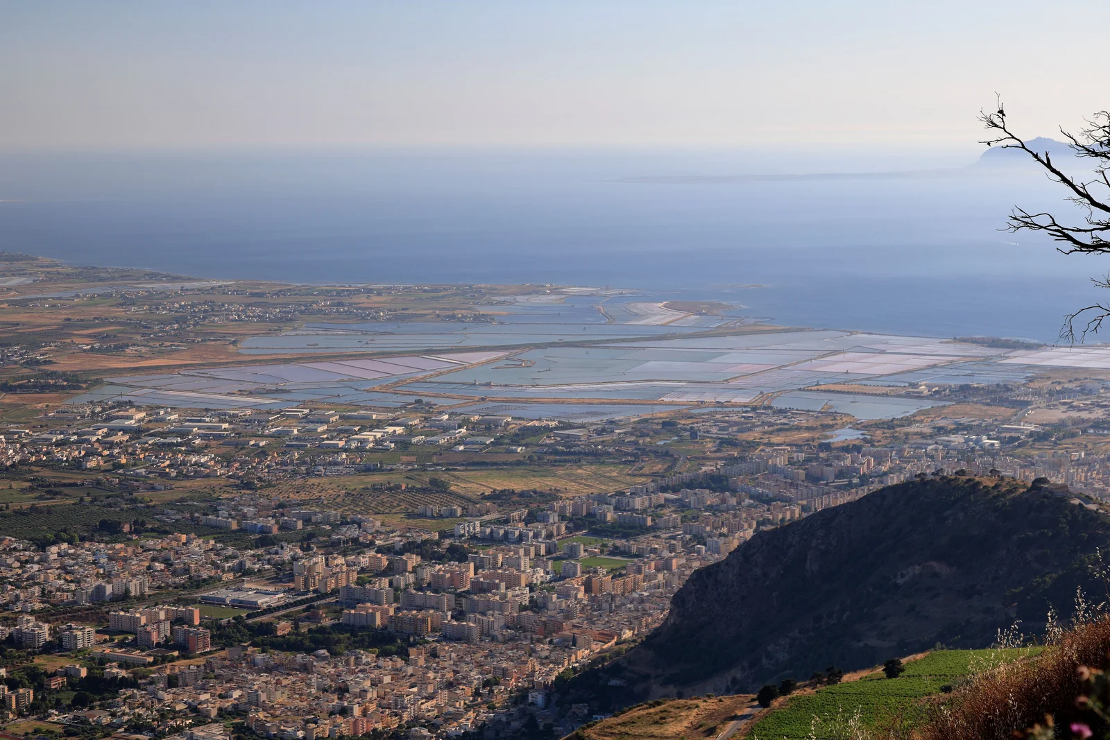 Aerial view of Trapani's coastline and salt pans in Sicily, seen from the hills above, with the sea in the background.
