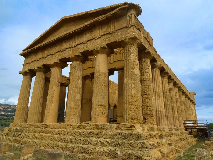 Stunning view of the Temple of Concordia, a well-preserved ancient Greek temple in Agrigento, Sicily, with golden stone, Doric columns, and a blue sky, shot from a low angle.