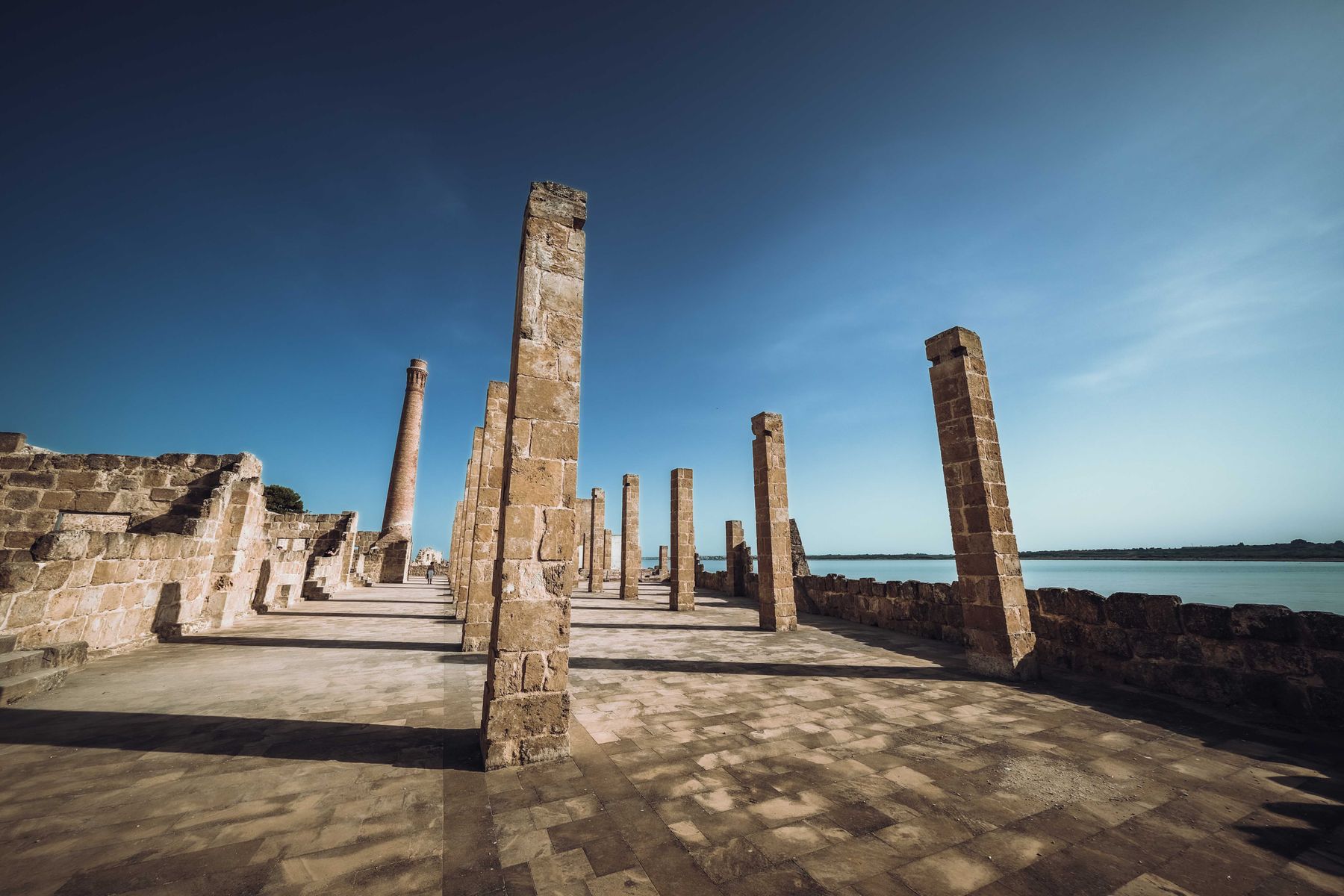 The ancient stone pillars of the Tonnara di Vendicari standing along the shoreline of the nature reserve under a clear blue sky.