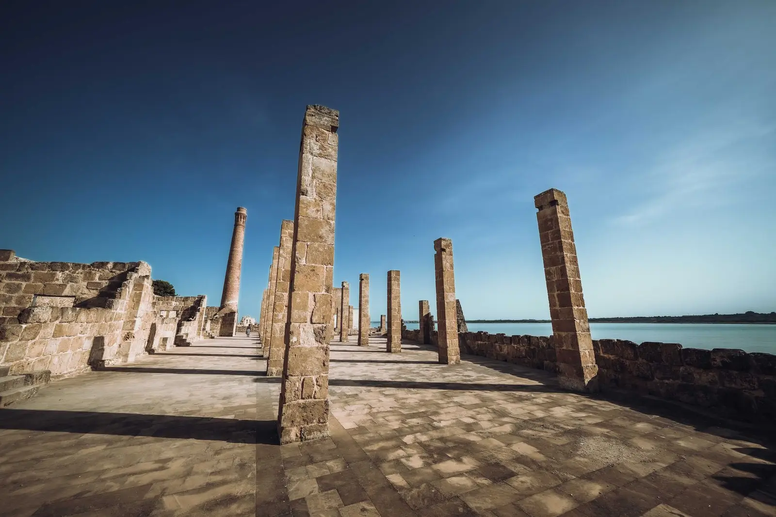 The ancient stone pillars of the Tonnara di Vendicari standing along the shoreline of the nature reserve under a clear blue sky.